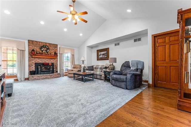 living room with ceiling fan, wood-type flooring, a wood stove, and high vaulted ceiling