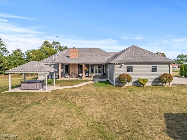 back of property with a lawn, a patio, and a hot tub