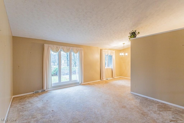 carpeted empty room featuring a textured ceiling and a notable chandelier