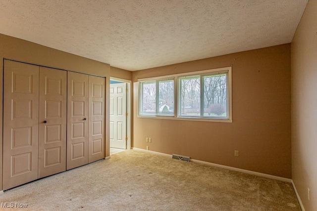 unfurnished bedroom featuring a textured ceiling, light colored carpet, and a closet