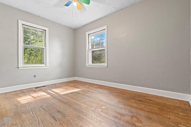 empty room with wood-type flooring, ceiling fan, a healthy amount of sunlight, and a textured ceiling