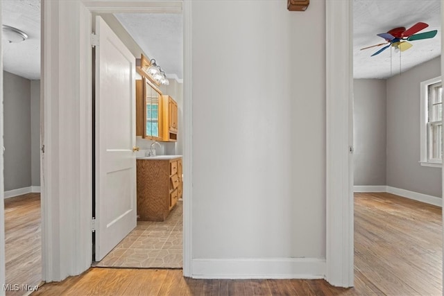 hall with a textured ceiling, light hardwood / wood-style floors, and sink