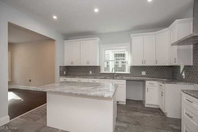 kitchen featuring white cabinets, a kitchen island, and wall chimney range hood