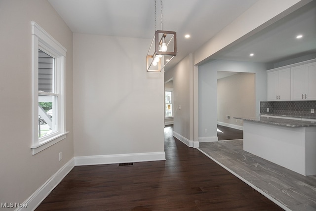 kitchen with white cabinets, pendant lighting, backsplash, dark wood-type flooring, and dark stone counters