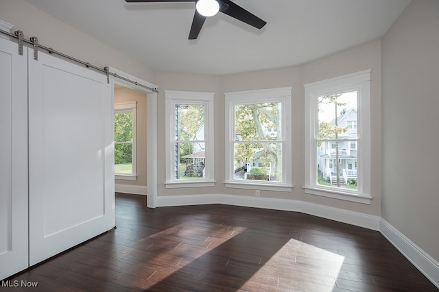 spare room featuring ceiling fan, dark wood-type flooring, and a barn door