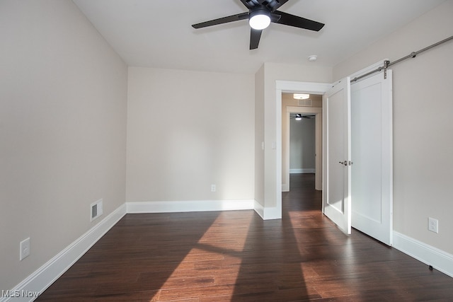 unfurnished room featuring ceiling fan, a barn door, and dark hardwood / wood-style flooring