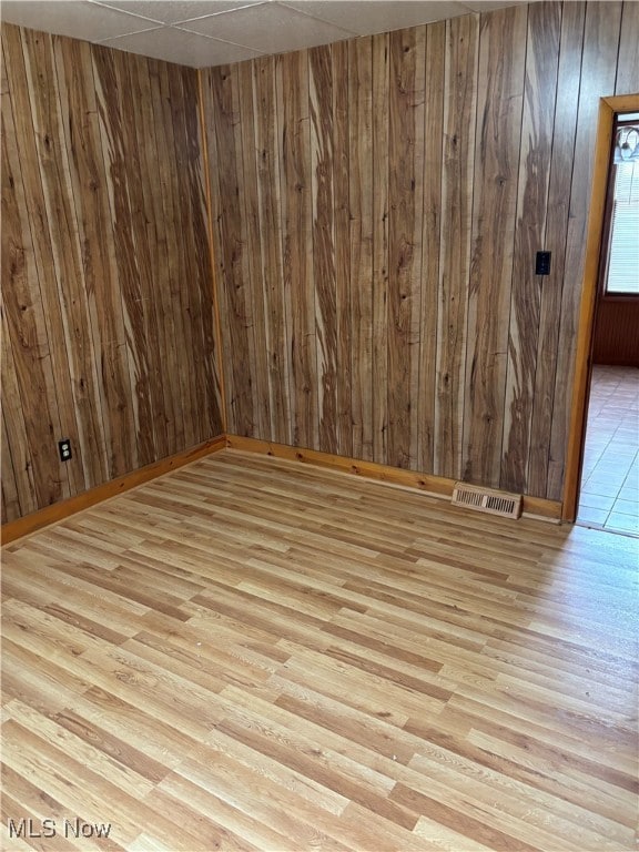 unfurnished room with light hardwood / wood-style flooring, wood walls, and a drop ceiling