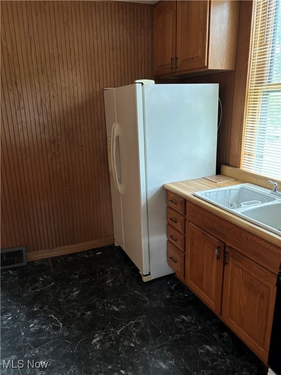 kitchen featuring white fridge with ice dispenser, wood walls, and sink