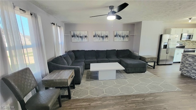 living room featuring light wood-type flooring, a textured ceiling, and ceiling fan