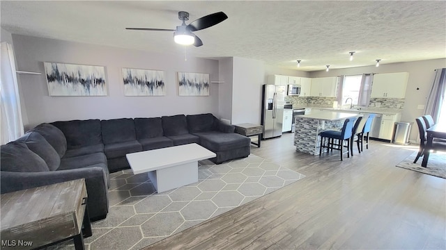 living room featuring light wood-type flooring, ceiling fan, sink, and a textured ceiling