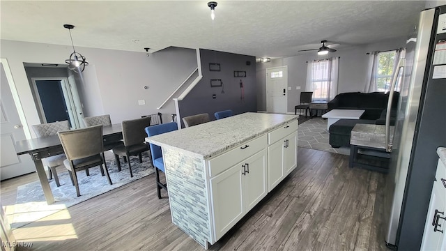 kitchen with pendant lighting, white cabinets, a kitchen island, stainless steel refrigerator, and ceiling fan