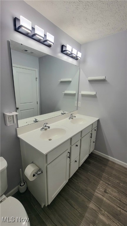 bathroom featuring a textured ceiling, wood-type flooring, vanity, and toilet