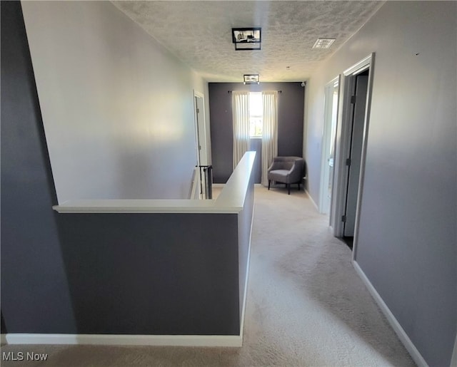 hallway with a textured ceiling and light colored carpet