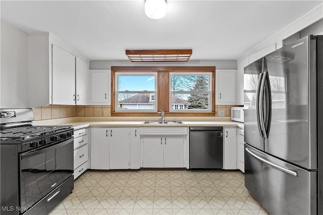 kitchen with light countertops, black range with gas stovetop, freestanding refrigerator, a sink, and dishwashing machine