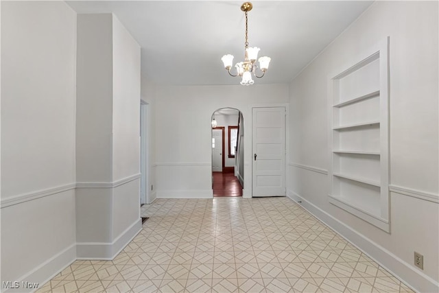 empty room with arched walkways, an inviting chandelier, baseboards, and built in features