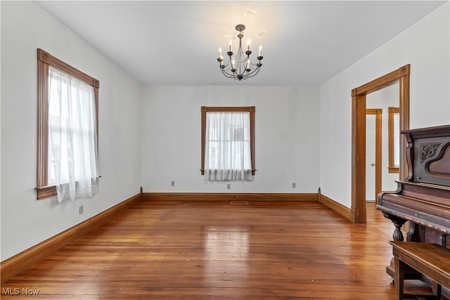 empty room with baseboards, hardwood / wood-style flooring, and a notable chandelier