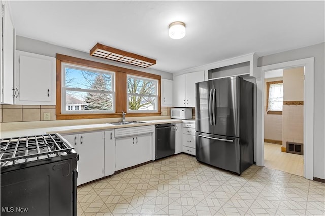 kitchen featuring light countertops, visible vents, white cabinets, a sink, and black appliances