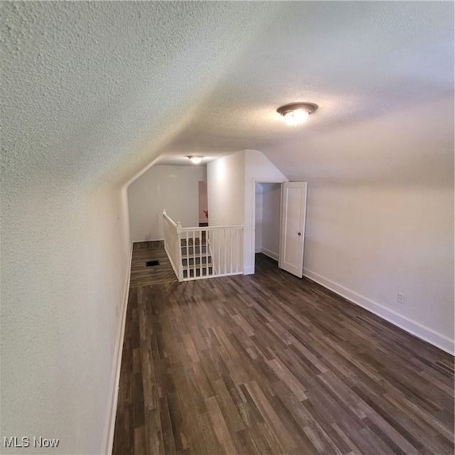 additional living space featuring a textured ceiling, lofted ceiling, and dark hardwood / wood-style flooring