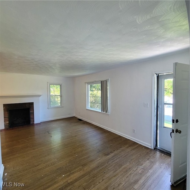 unfurnished living room with dark hardwood / wood-style floors and a brick fireplace