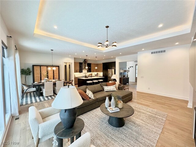 living room with a notable chandelier, a raised ceiling, light wood-type flooring, and a textured ceiling