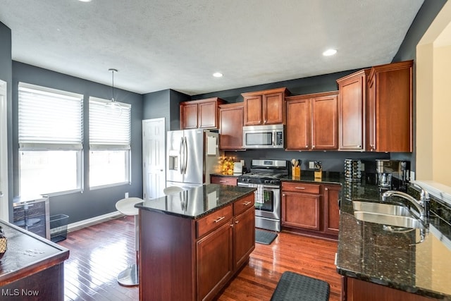 kitchen with appliances with stainless steel finishes, hanging light fixtures, dark wood-type flooring, and a center island