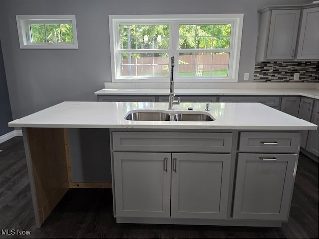 kitchen featuring sink, a center island with sink, backsplash, dark wood-type flooring, and gray cabinets