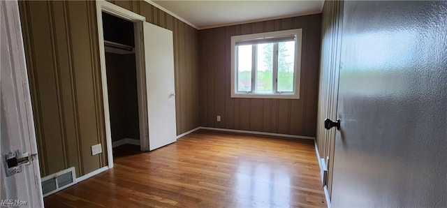 unfurnished bedroom featuring wood-type flooring, wooden walls, a closet, and ornamental molding