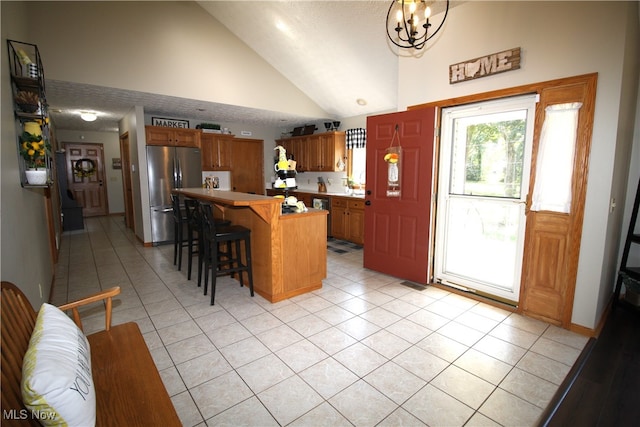 kitchen featuring stainless steel refrigerator, a kitchen bar, high vaulted ceiling, and light tile patterned flooring