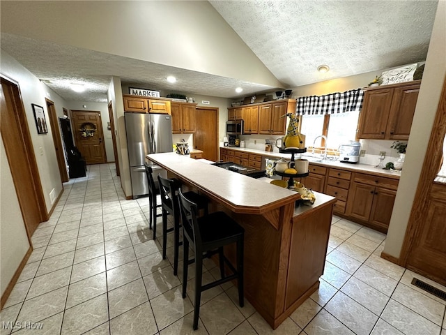 kitchen with a textured ceiling, a breakfast bar area, vaulted ceiling, a kitchen island, and appliances with stainless steel finishes