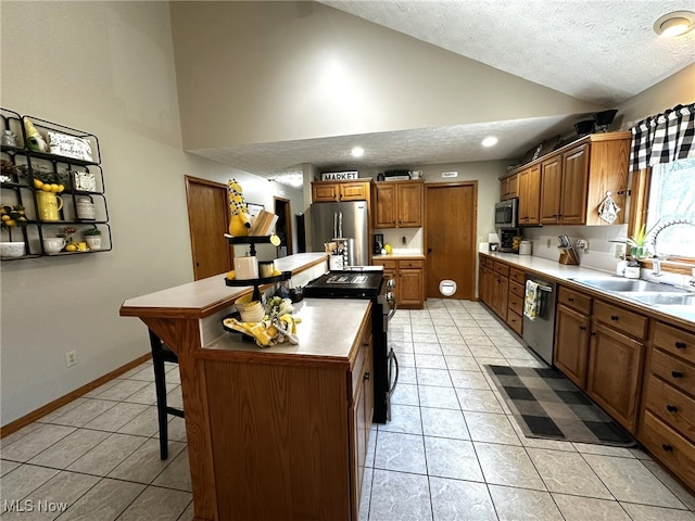 kitchen featuring appliances with stainless steel finishes, a breakfast bar, a kitchen island, a textured ceiling, and sink