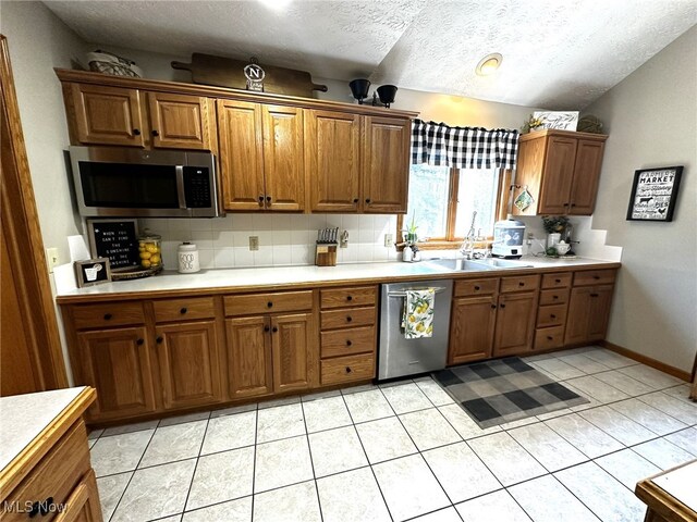 kitchen featuring lofted ceiling, light tile patterned floors, a textured ceiling, appliances with stainless steel finishes, and decorative backsplash