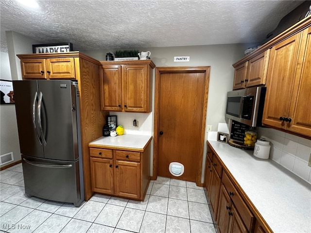 kitchen featuring a textured ceiling, backsplash, light tile patterned floors, and stainless steel appliances