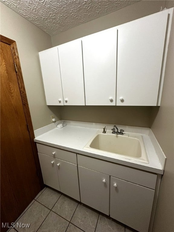 laundry area featuring light tile patterned floors, a textured ceiling, and sink