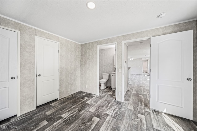 unfurnished bedroom with ornamental molding, a textured ceiling, dark hardwood / wood-style floors, and ensuite bathroom