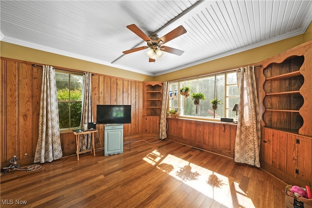 unfurnished living room featuring ceiling fan, wooden walls, plenty of natural light, and dark wood-type flooring