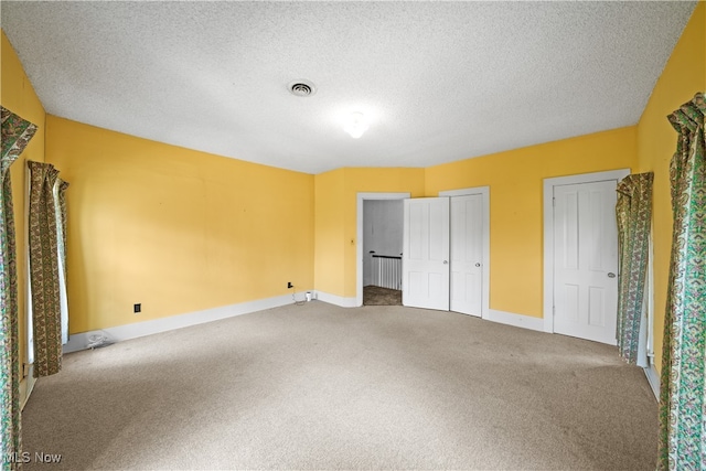 unfurnished bedroom featuring a textured ceiling, carpet, and multiple closets