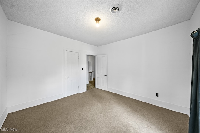 spare room featuring dark carpet and a textured ceiling