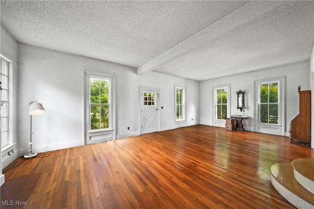 unfurnished living room with a textured ceiling, beamed ceiling, and hardwood / wood-style flooring