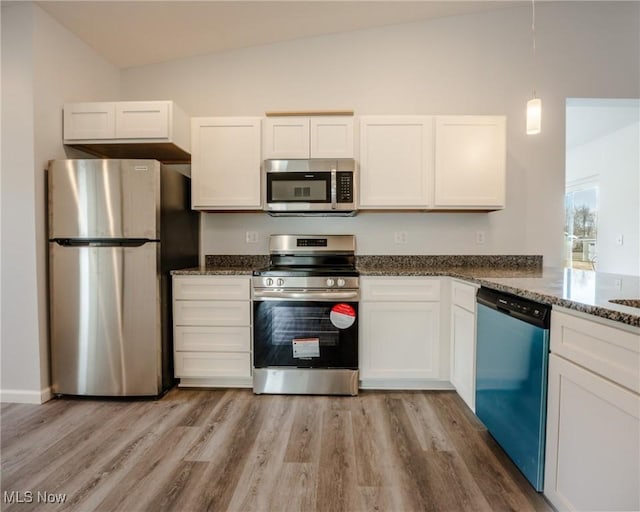 kitchen with appliances with stainless steel finishes, light wood-type flooring, dark stone counters, decorative light fixtures, and white cabinets