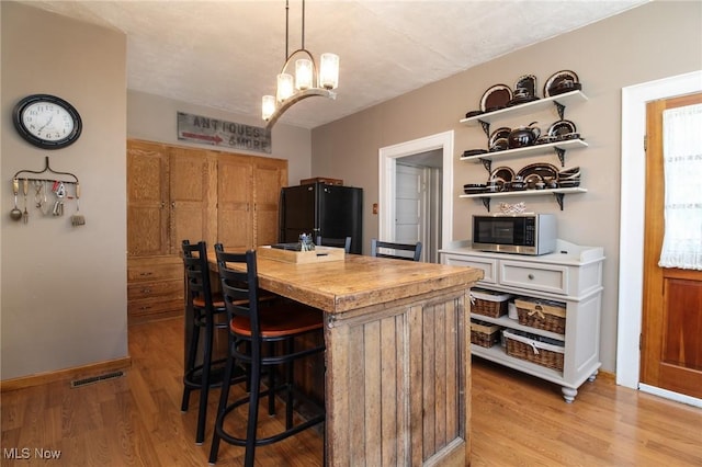 kitchen featuring black refrigerator, light wood-type flooring, an island with sink, and a breakfast bar area