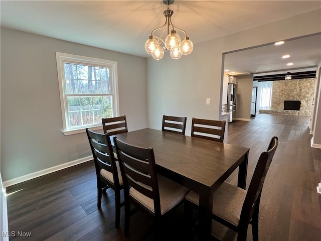 dining area with a stone fireplace, a notable chandelier, and dark hardwood / wood-style floors