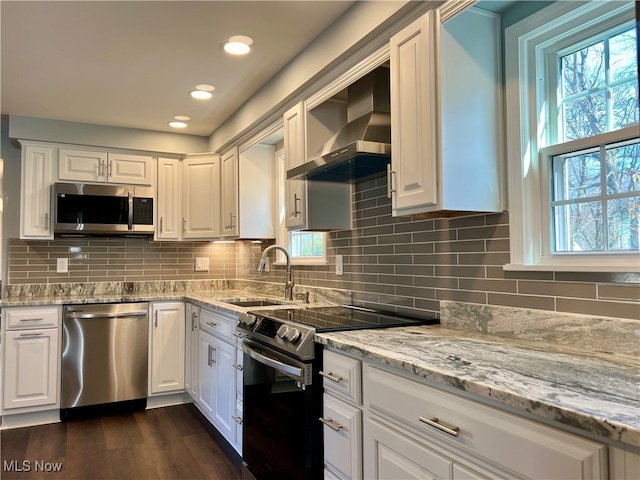 kitchen with appliances with stainless steel finishes, white cabinetry, backsplash, dark hardwood / wood-style flooring, and wall chimney range hood