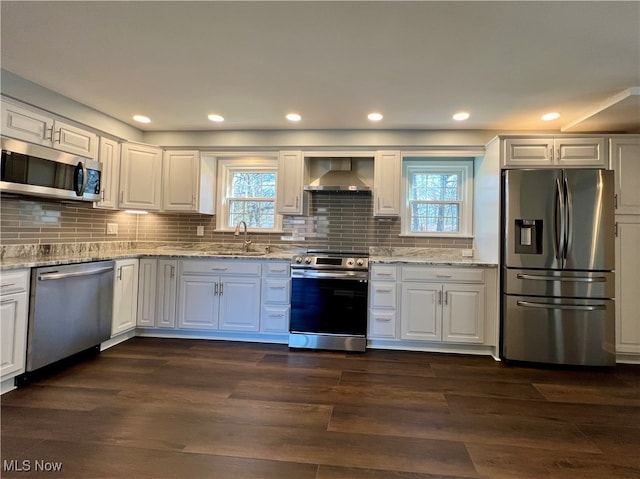 kitchen with white cabinets, stainless steel appliances, wall chimney exhaust hood, and dark wood-type flooring