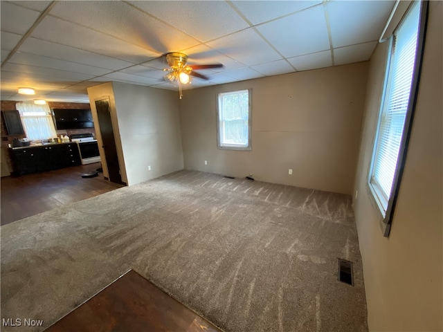 unfurnished living room with ceiling fan, a paneled ceiling, and dark carpet