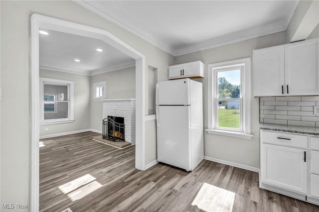 kitchen with white cabinetry, light hardwood / wood-style flooring, a brick fireplace, and white refrigerator