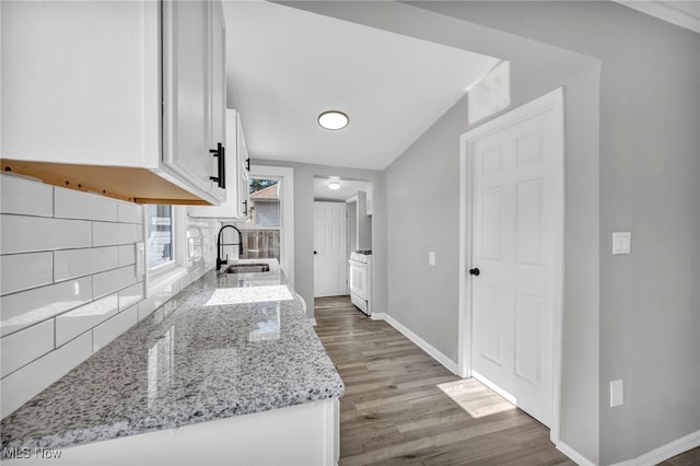 kitchen with light stone counters, white cabinets, lofted ceiling, hardwood / wood-style floors, and sink