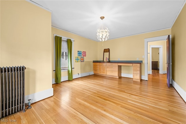 spare room with built in desk, light hardwood / wood-style floors, radiator heating unit, and a notable chandelier