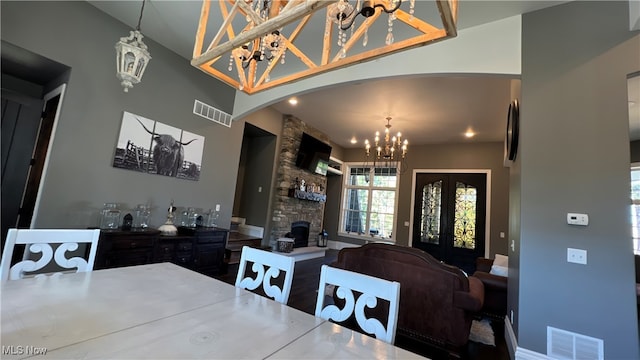 dining space with french doors, a stone fireplace, and a chandelier