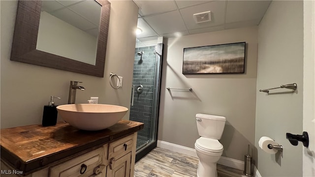 bathroom featuring toilet, a shower with shower door, wood-type flooring, vanity, and a paneled ceiling