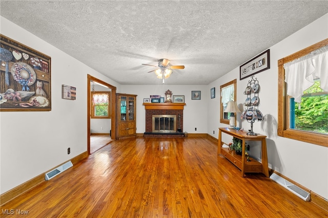 unfurnished living room with a brick fireplace, wood-type flooring, a healthy amount of sunlight, and a textured ceiling